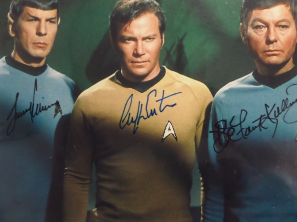 This 1967 color 8x10 shows Kirk, Spock and another crew member from the hit sci-fi TV series., It comes hand signed by DeForrest Kelley, deceased Leonard Nimoy, and the very tough William Shatner in black and blue sharpies. Grades are all strong 9's, and value is about a grand. 