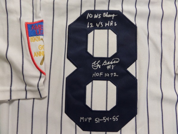 This home white NYY throwback pinstriped jersey from Mitchell & Ness is a size L that comes to us in NM/MT condition, trimmed in navy, and with everything sewn.  It is back number-signed in silver paint pen by the all time great catcher himself, grading an overall 9 with 10WS Champ, 12 WS HR's, HOF 1972 and MVP 51-54-55 inscriptions, and this jersey is worth thousands!