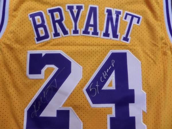 This yellow size 50 Kobe Bryant #24 Los Angeles Lakers jersey is like new, and comes trimmed in purple and white, with everything sewn.  It is hand-signed in his full name on the back number in silver sharpie by the all time great himself, as well as a super cool 5X Champ inscription, and with his 2020 death, this amazing looking jersey is valued well into the low thousands!
