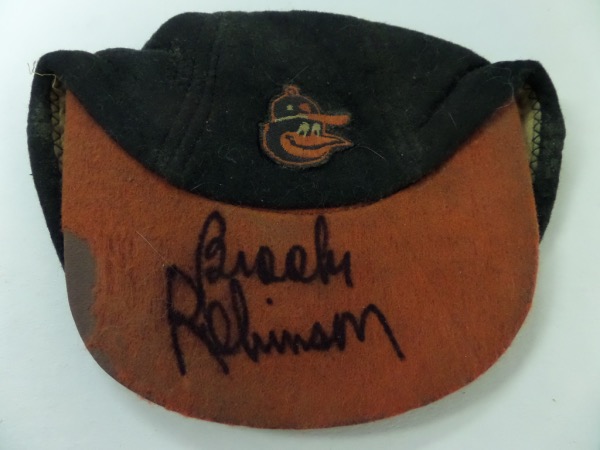 This black Baltimore Orioles cap features a team logo and an orange brim, and is in Fair overall condition, showing quite a bit of wear and age.  We do not know if this was actually worn in a game by an O's player, but it more than likely is from the 1950's, and it comes hand-signed on said brim in bold black sharpie by 16 time GG winner and HOF 3B, Brooks Robinson.  This is a fabulous signature, grading an 8 at least, and retail on this gorgeous and very old item is mid hundreds!