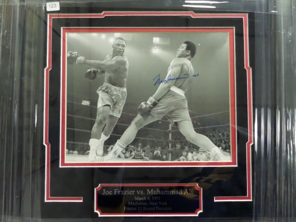 This 18x18 square professionally-framed and double-matted display features a custom-engraved nameplate and a black and white image of the 1971 "Fight of the Century" between Joe Frazier and Muhammad Ali.  The photo is hand-signed in blue sharpie by Ali, grading a strong 8.5, and this display-ready framed piece is valued into the low thousands!