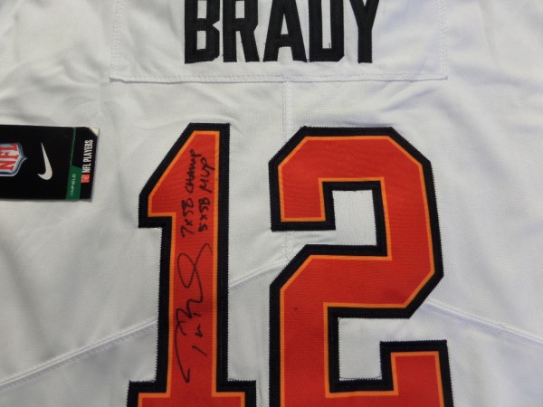 This white size L Tampa Bay Bucs #12 Tom Brady jersey is from Nike, and comes to us still tagged as NEW.  It has everything sewn, and is back number-signed in black by the future HOF passer himself.  The signature is a nice 8 at least, complete with 7X SB Champ and 5X SB MVP inscriptions, and retail right now is THOUSANDS on this jewel!
