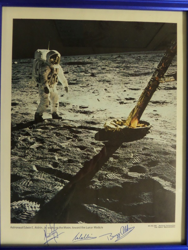 This 12x15 blue-framed display features a color photo from NASA, featuring an image of Buzz Aldrin walking the moon in his spacesuit.  It is hand-signed at the bottom in blue by all three groundbreaking, moon-landing men, including Neil Armstrong, Michael Collins, and Aldrin himself.  The signatures grade clean 9's or better, and this display-ready piece is valued into the low thousands!