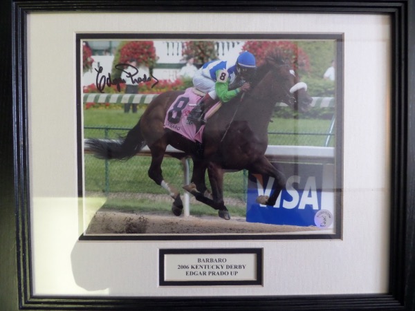 This 13x16 professionally-framed and double-matted display features a color image of Edgar Prado riding stud horse Barbaro to the 2006 Kentucky Derby crown.  It is hand-signed in black sharpie by Prado himself, grading a strong 8.5, and the piece comes with a COA and hologram from Bugboys.com for absolute authenticity.  Ready for display, and a MUST for any racing collection!
