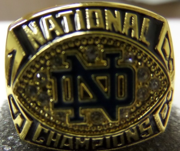 This incredibly well done ring is a beauty. it is dated from the 1988 National Championship squad and some say, the greatest Fighting Irish team ever to suit up. It is a superb ring, made of celestrium and gold plated. It has the blue "ND" logo in the center, surrounded by brilliant CZ diamonds, and has Coach Lou Holtz's name on one shank, with the team record engraved on the other. It is a must have ring, not a cheap lightweight copy, not a fans ring, and not a cheap special on Ebay. Great chance, great reserve price, and value is truly ,HIGH on this Notre Dame Stunner..