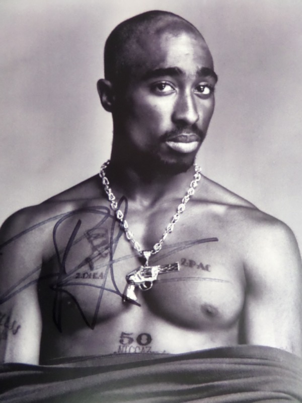 This black and white 8.5x11 photo shows Hip Hop music icon Tupac Shakur standing shirtless and staring into the camera.  It is hand-signed in black sharpie by the rapper/actor himself, the signature grading a legible 7.5-8 overall, and with his death now more than two and a half decades back, retail is well into the hundreds!