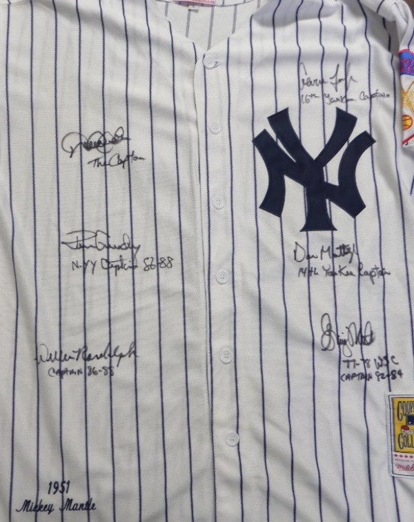 This home white, pinstriped size L New York Yankees jersey from Mitchell & Ness is a 1951 Mickey Mantle #7 throwback that comes to us in NM condition, with everything sewn.  it is front-signed in black sharpie by 6 different Yanks captains that took over after Thurman Munson.  They include Graig Nettles, Ron Guidry, Willie Randolph, Don Mattingly, Derek Jeter and Aaron Judge.  Signatures are 8's or better, each with an inscription, and this unique NYY jersey is valued into the low thousands!