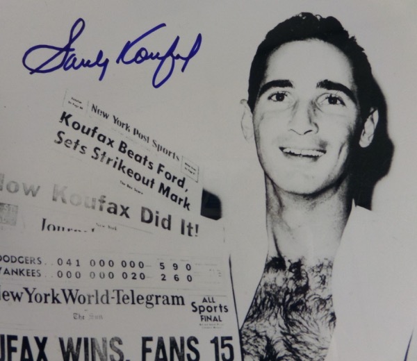 This black and white 8x10 photo shows Sandy Koufax holding up newspapers announcing his 15 strikeout performance in the '63 Series.  It is hand-signed in blue sharpie by the dominant HOF lefty himself, and the photo comes with a COA from Ideal Autographs.  A very tough autograph to obtain these days, and the prices certainly reflect that!