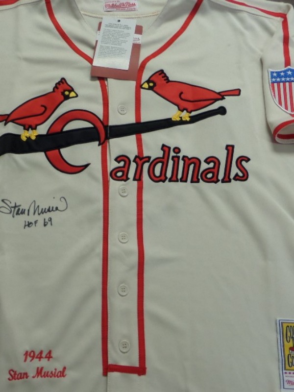 This cream-colored size L St. Louis Cardinals 1944 throwback from Mitchell & Ness is still in NM condition, with everything sewn.  It is back number-signed in black sharpie by the 3 time NL MVP and HOF great himself, grading a legible 8, with a HOF 69 inscription.  Valued into the mid/high hundreds!