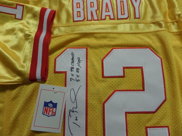 This bright orange size 50 Tampa Bay Bucs #12 Tom Brady throwback jersey is from Mitchell & Ness, and comes with original tagging attached.  It has everything sewn, and is back number-signed in black by the future HOF passer himself.  The signature is a nice 8 at least, complete with 7X SB Champ and 5X SB MVP inscriptions, and retail right now is THOUSANDS on this jewel!