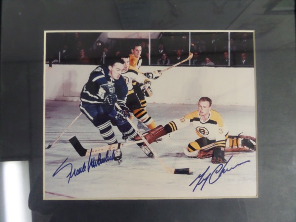 This 12x15 framed and matted display houses a color action photo of a Maple Leafs/Bruins game, in which Bruins goalie Garry Cheevers is challenging a charge by Maple Leafs' Frank Mahovlich.  It is hand-signed in blue felt tip marker by both HOF greats, is 100% display-ready, and retail is mid hundreds with a Shooting Star Memorabilia COA included!