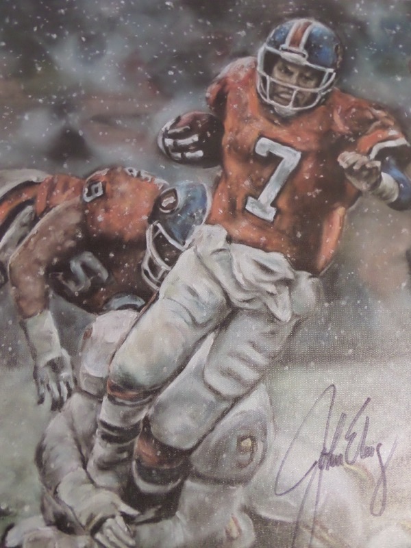 This full color 18x22 artist's litho print is done on canvas, and features a beautiful artist's image of John Elway as a member of the Denver Broncos, for whom he played his entire career and won 2 Super Bowls.  It is a very striking litho, comes boldly black sharpie-signed by the HOF passer himself, and will frame and display proudly in any collection.  Valued well into the hundreds!