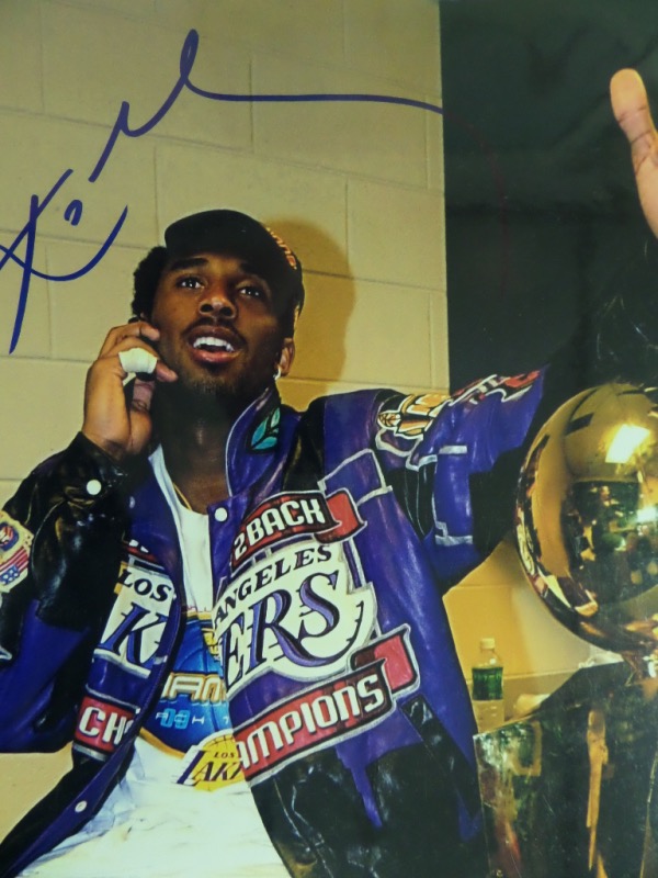 This colorful 11x14 photo shows Kobe Bryant postgame, wearing a Lakers Champions jacket, and sitting next to the Naismith Memorial Trophy, given to the NBA Champions.  It is hand-signed in blue sharpie, reading just his first name, but grading a clean, bold 9 at least, and with Kobe now gone 4 years, retail is low thousands!