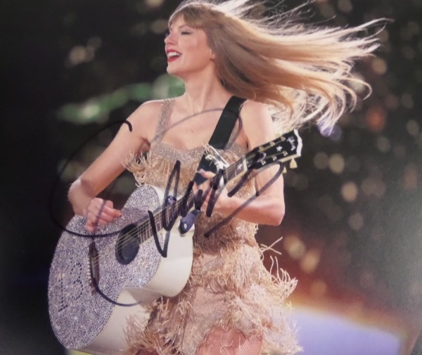 This full color 8.5x11 photo shows Taylor in concert, and comes black sharpie-signed by the country/pop superstar herself.  Signature grades about a 7 overall, and will show off from across a room when this baby is framed for display.  Valued well into the hundreds on the retail circuit!