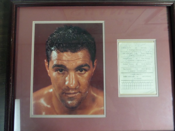 This vintage double matted and wood framed wall hanging looks to have been put together about 1992 or so and measures near 16x20 in size. It holds a large color photo of the long deceased HOF champ, as well as a hand signed judges scorecard from his fight with Don Cockell. Cool display, and value is upper hundreds. 