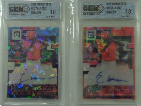 This fantastic twofer is TWO different 2022 Donruss Optic Elly De La Cruz Rated Prospect rookie baseball cards, each slabbed a Gem Mint 10 from the GEM grading company, and each penned in blue sharpie by the Reds rookie star.  Sell one, keep one, and still make out!