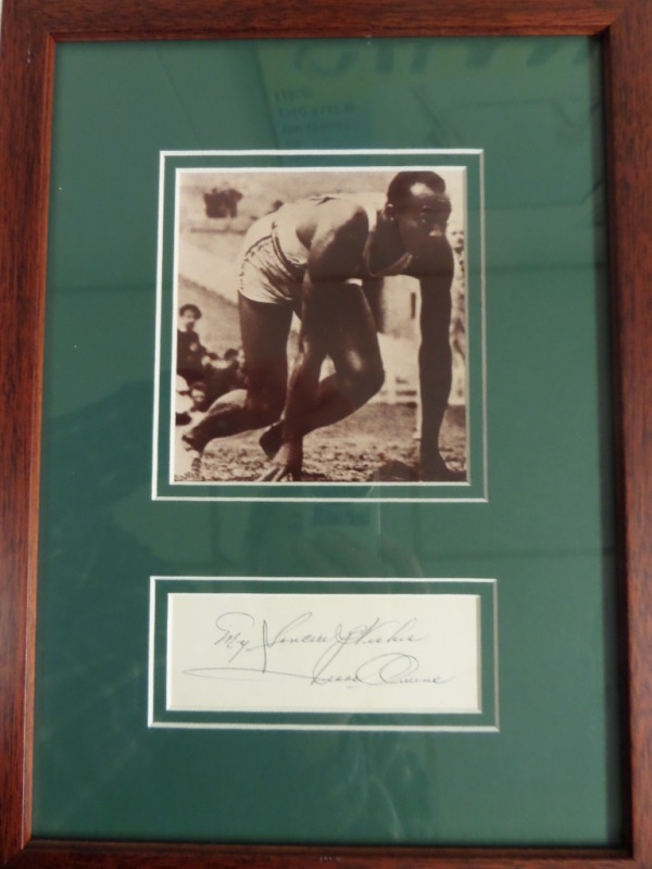 This wood-framed and green-matted 10x14 professionally-done display features a black and white 1936 Olympics photo of Jesse Owens on the blocks before a race.  There is a cut matted below the photo, hand-signed in blue ink by the track legend himself, and this display-ready piece is valued well into the hundreds!