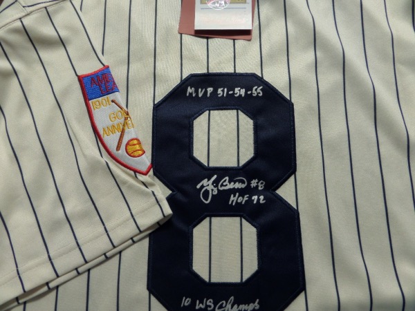 This home white NYY 1951 throwback pinstriped jersey from Mitchell & Ness is a size L that comes to us tagged as new, trimmed in navy, and with everything sewn.  It is back number-signed in silver paint pen by the all time great catcher himself, grading an overall 9 with #8, HOF 1972, 10X WS Champs, and MVP 51-54-55 inscriptions, and this jersey is worth thousands!