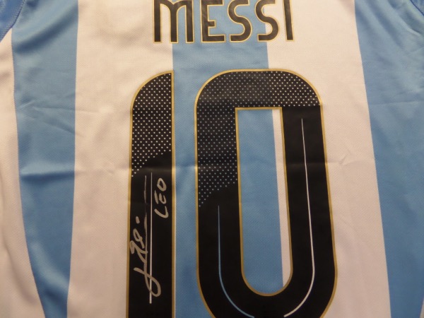 This blue size M AFA soccer jersey is still NEW with tags, and comes back number-signed in bright silver paint pen by one of the finest soccer players in the world today, Lionel Messi.  The bright signature grades a legible 8.5 overall, complete with his standard LEO inscription, and the jersey easily values well into the hundreds!