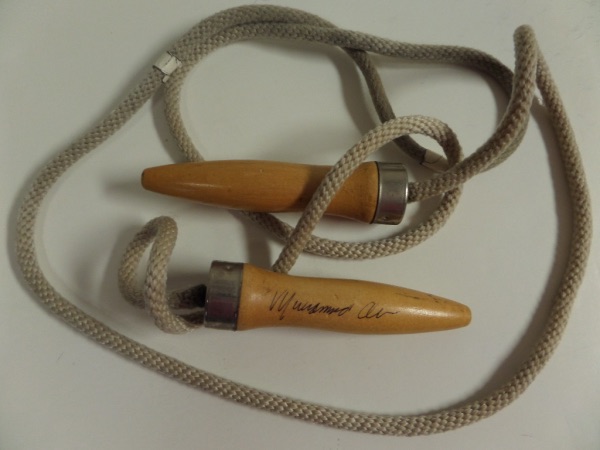 This vintage actual rope and wood handle jump rope is still in EX condition overall.  It is hand-signed in black ink against one of the handles by "The Greatest" himself, 3 time Heavyweight Champion, Muhammad Ali, and though this is a TOUGH surface to sign, the autograph still grades about a 7--please see our attached photo.  A super cool, super unique, and high value collector's item!